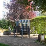 Garten mit Liege, Tisch, Stühlen und Grill. Hinterhof mit Bäumen und Hecke.