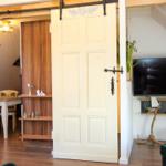 Raum mit Schiebetür, Fernseher und Holzmöbeln. Decke mit Sparren und Wanddekoration.
