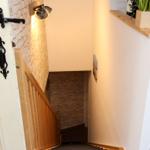 Helle Treppe mit Holzgeländer und Steinwand. Tür mit schwarzen Metallgriffen.