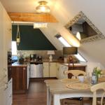 Küche mit Essbereich unter Dachschräge, Holztisch, Stühle, Spüle, Dunstabzug und Fenster.