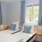 Zimmer mit Doppelbett, zwei Fenstern und Holzsideboards mit Lampen.