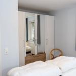 Schlafzimmer mit Bett, Kleiderschrank und Fenster mit Vorhängen.