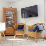 Zwei Rattan-Stühle mit Kissen, Fernseher und Essbereich mit Holztisch und weißen Stühlen.