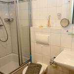 Badezimmer mit Dusche, Waschbecken und Toilette. Fliesenwand, Spiegel und Handtuch.