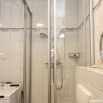 Badezimmer mit Dusche, Waschmaschine und runden Spiegel.