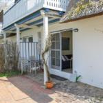 Wohnung mit Terrasse, Gartentisch und Schiebetür. Dach aus Stroh, weißer Putz, Pflanzen.