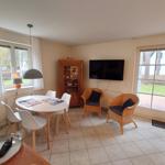 Essbereich mit Tisch und Stühlen, Fernseher und zwei Rattan-Stühle an der Wand.