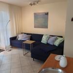 Ein Wohnzimmer mit blauem Sofa, Fenstern und Wandbild.