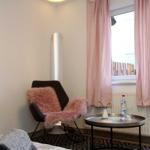 Ein Raum mit einem Stuhl, rosa Fell und einem Tisch vor einem Fenster mit rosa Vorhängen.