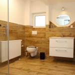 Badezimmer mit Holzoptik, Waschtisch, Toilette und Dusche mit Glaswand.