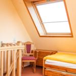 Zimmer mit Dachschrägen, Dachfenster, Bett, Stuhl und Schrank.