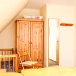 Schlafzimmer mit Holzschrank, Kinderbett und Spiegel an der Wand.