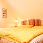 Schlafzimmer mit Bett, Nachttisch und Lampe unter schrägem Dach.