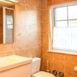 Badezimmer mit Waschbecken, Toilette und Dusche. Fenster mit weißen Vorhängen.