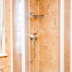 Dusche mit Glaswand, Duschbrause und Heizkörper an der Wand.