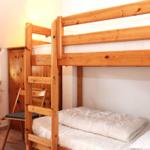 Ein Raum mit einem Holz-Etagenbett, einem Stuhl und einem Fenster mit Vorhang.