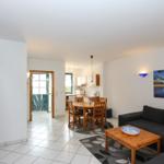 Wohnbereich mit Sofa, Esstisch und Küchenbereich. Holztür und Wandbild sichtbar.