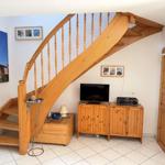 Holztreppe führt zur oberen Etage. Fernseher und Kabinett stehen im Raum.