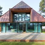 Moderne Villa mit Glasfassade und Holzverkleidung, umgeben von Bäumen und Grünfläche.