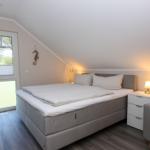 Schlafzimmer mit Doppelbett, Nachttisch und Sessel. Fenster mit Blick auf Außenbereich.