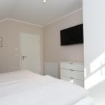 Schlafzimmer mit Bett, Kleiderschrank und Fernseher an der Wand.