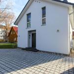 Moderne weiße Villa mit Eingangstür und gepflastertem Hof.