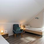 Zimmer mit zwei Betten, Stuhl und Fenster. Holzboden und schräges Dach.