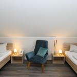 Zwei Einzelbetten und ein Sessel mit Beistelltischen und Lampen.