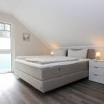 Schlafzimmer mit Doppelbett, Nachttisch und Fenster. Holzfußboden und schräge Decke.