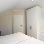 Schlafzimmer mit Dachschrägen, Bett, Kleiderschrank und Fernseher an der Wand.
