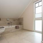 Badezimmer mit Badewanne, Dusche und Fenster. Wand- und Bodenfliesen in neutralen Tönen.
