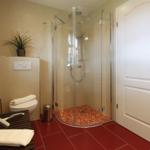 Badezimmer mit Dusche, Toilette und Badewanne. Bodenfliesen rot, Wandfliesen beige.