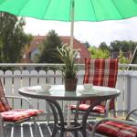 Terrasse mit Tisch, drei Stühlen und grünem Sonnenschirm. Hintergrund: weiße Zaun und Häuser.