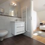 Badezimmer mit Toilette, Waschbecken und Heizkörper. Durchgang zur Schlafzimmer.
