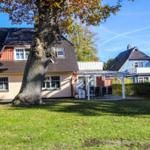 Haus mit großem Garten und Terrasse unter einem großen Baum.