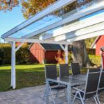 Terrasse mit Glasdach, Tisch und Stühlen. Hintergrund: rote Scheune und Baum.