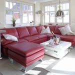 Ein Wohnzimmer mit rotem Ledersofa, weißem Couchtisch und großen Fenstern.