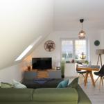 Wohn- und Essbereich mit Sofa, TV und Tisch. Dachschräge, Fenster und Wand mit Muster.