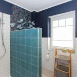 Bad mit Dusche, Fenster und Holzregal. Wände mit blauen und weißen Fliesen.