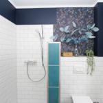 Duschbereich mit weißen Fliesen, blauem Wandpaneel und floraler Tapete. Dusche mit Handbrause und Toilette.