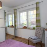 Schlafzimmer mit Bett, Kleiderschrank, Sessel und TV. Fenster mit Vorhängen.