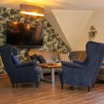 Wohnzimmer mit Sofa, zwei blauen Sesseln und Fernseher an floraler Wand.