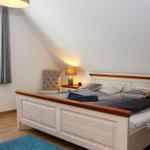 Schlafzimmer mit Bett, Nachttisch, Stuhl und Fenster.