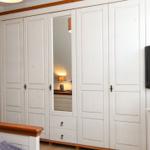 Schlafzimmer mit weißem Schrank, Spiegeltür und Fernseher auf Holzregal.