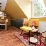 Wohn- und Essbereich mit gelbem Sessel, Holztisch und Terrakottaboden unter schrägem Dach.