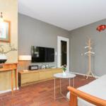 Wohnzimmer mit Fernseher, Couch, Kleiderständer und Wanddekoration