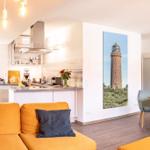Wohnküche mit Sofa, Esstisch und Leuchten. Wandbild zeigt einen Leuchtturm.