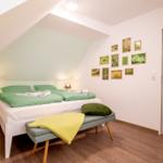 Schlafzimmer mit Doppelbett, grüner Bettwäsche und Holzboden unter schrägem Dach