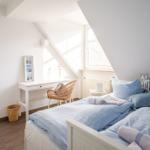 Zimmer mit Doppelbett, Schreibtisch und Fenster unter Dachschräge.