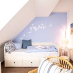 Schlafzimmer mit Dachschrägen, Bett mit Kissen und Wanddekoration.